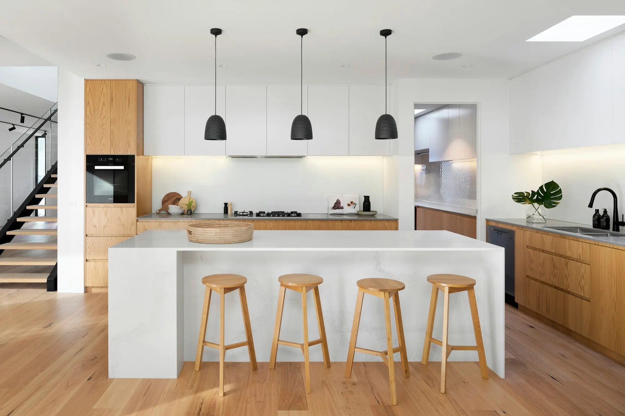 Bright white kitchen with a quartz island, oak floors and three wooden stools