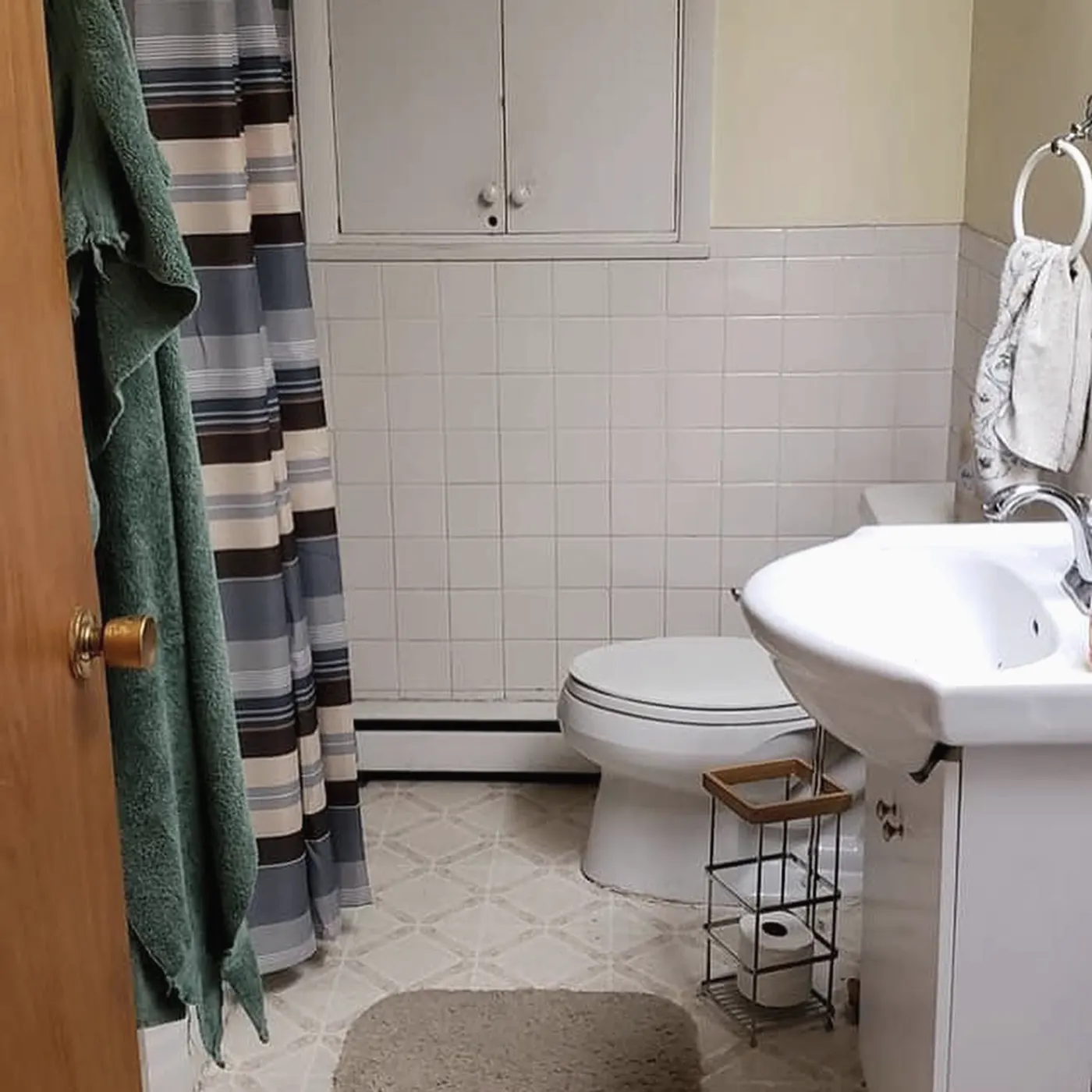 Before: small bathroom with a pedestal sink, patterned vinyl floor and striped shower curtain