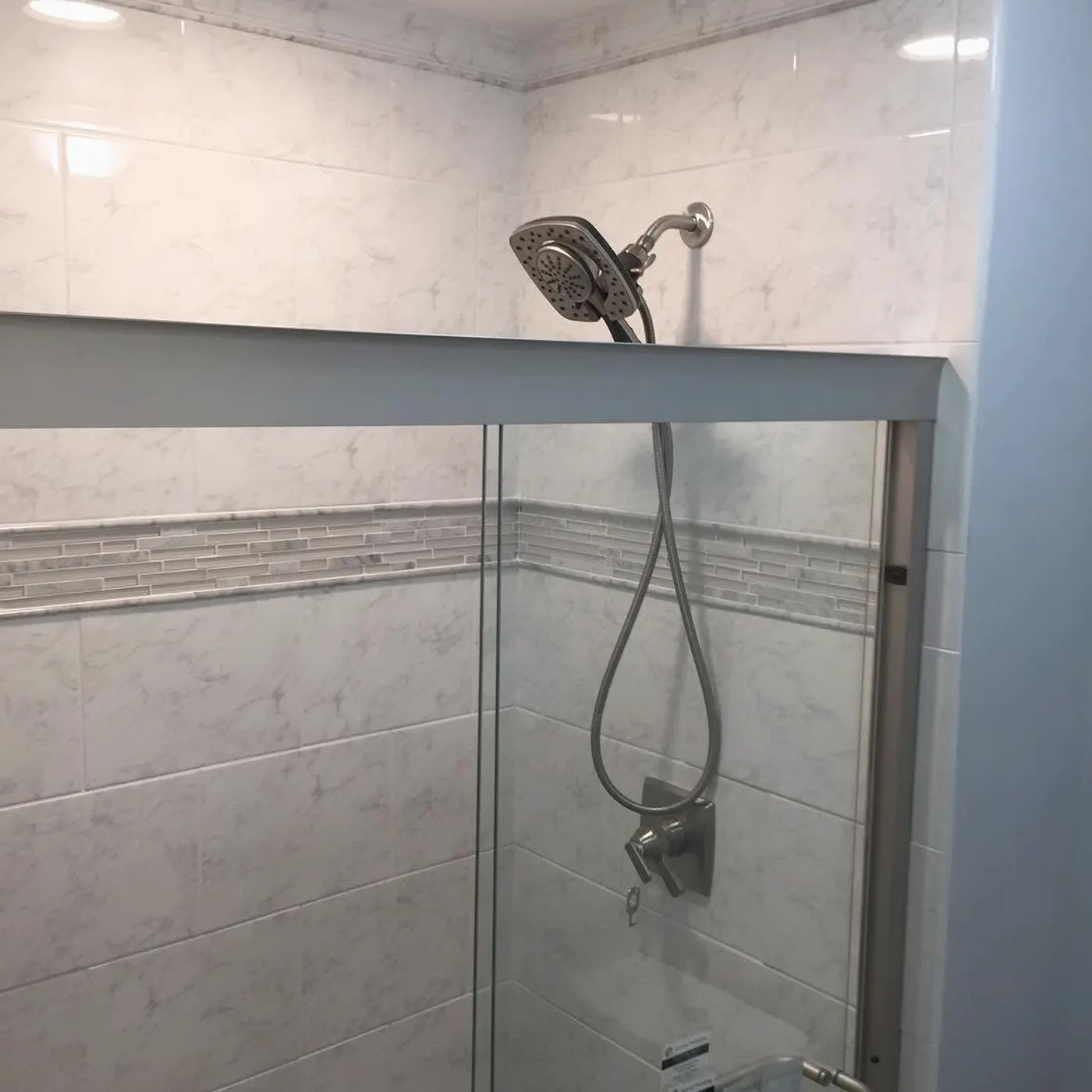 Walk-in shower in marble-look tile with a mosaic band and glass door