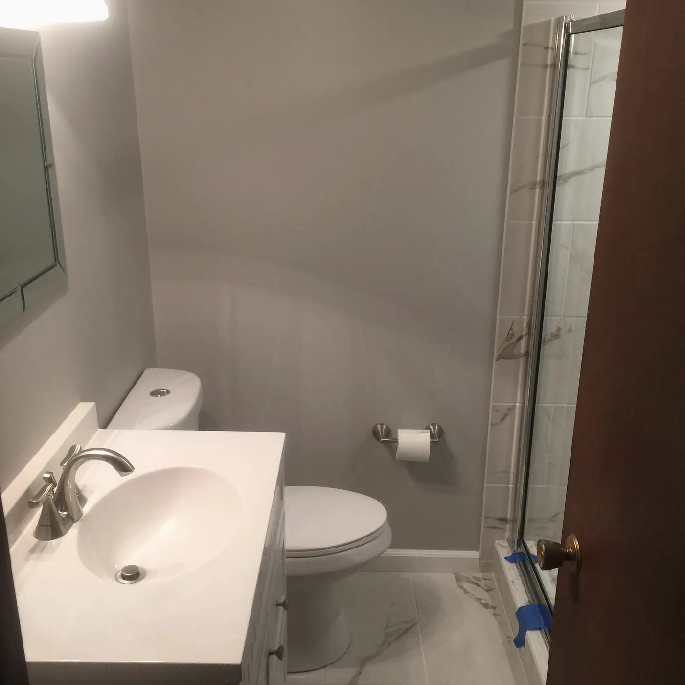 Small bathroom with new vanity and toilet, shower door being fitted