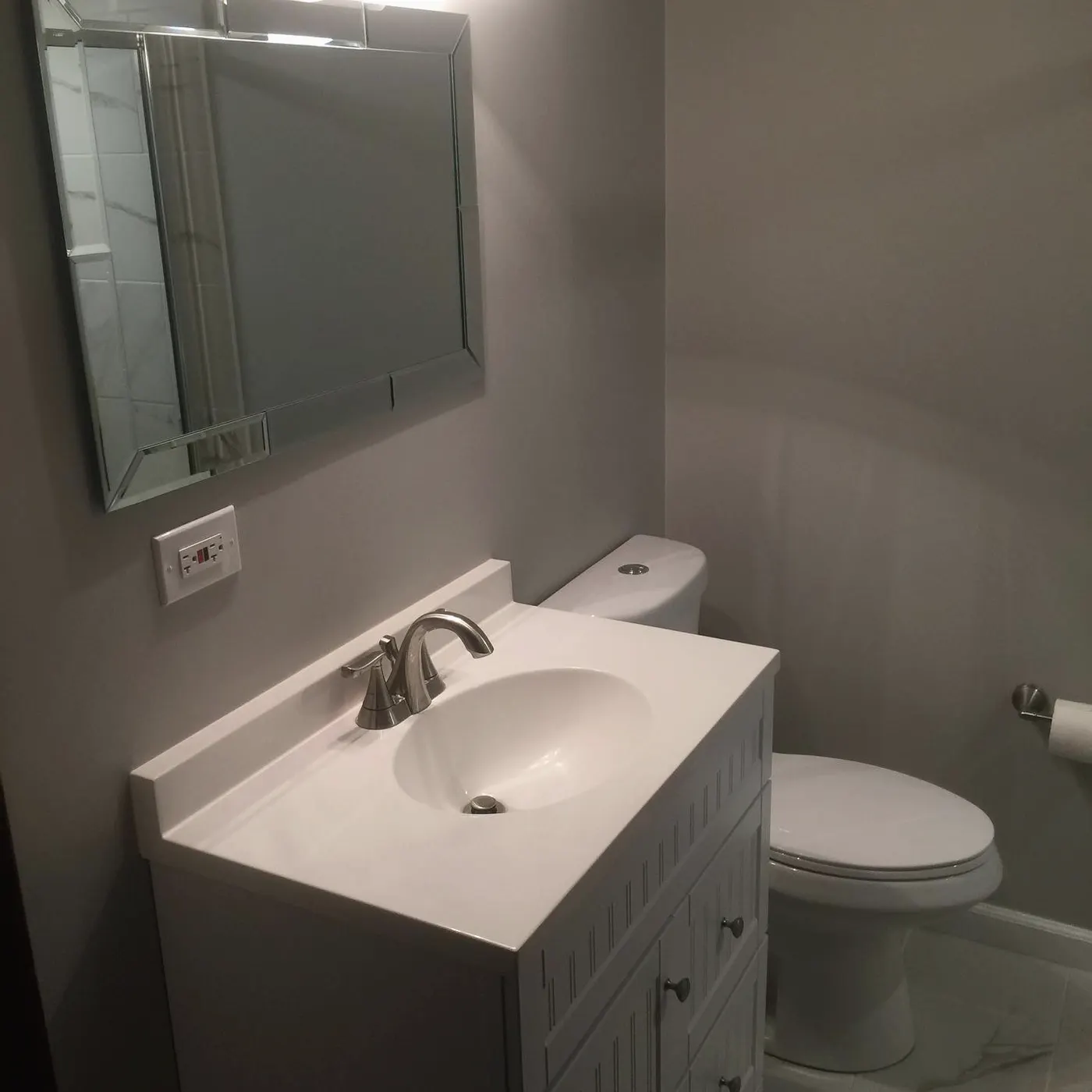 Finished small bathroom with a white vanity, framed mirror and grey walls