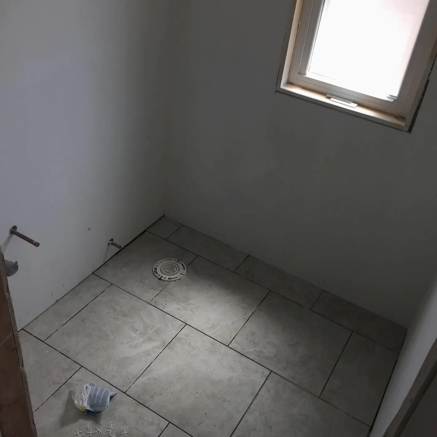 Room with new large-format tile floor being finished, window above