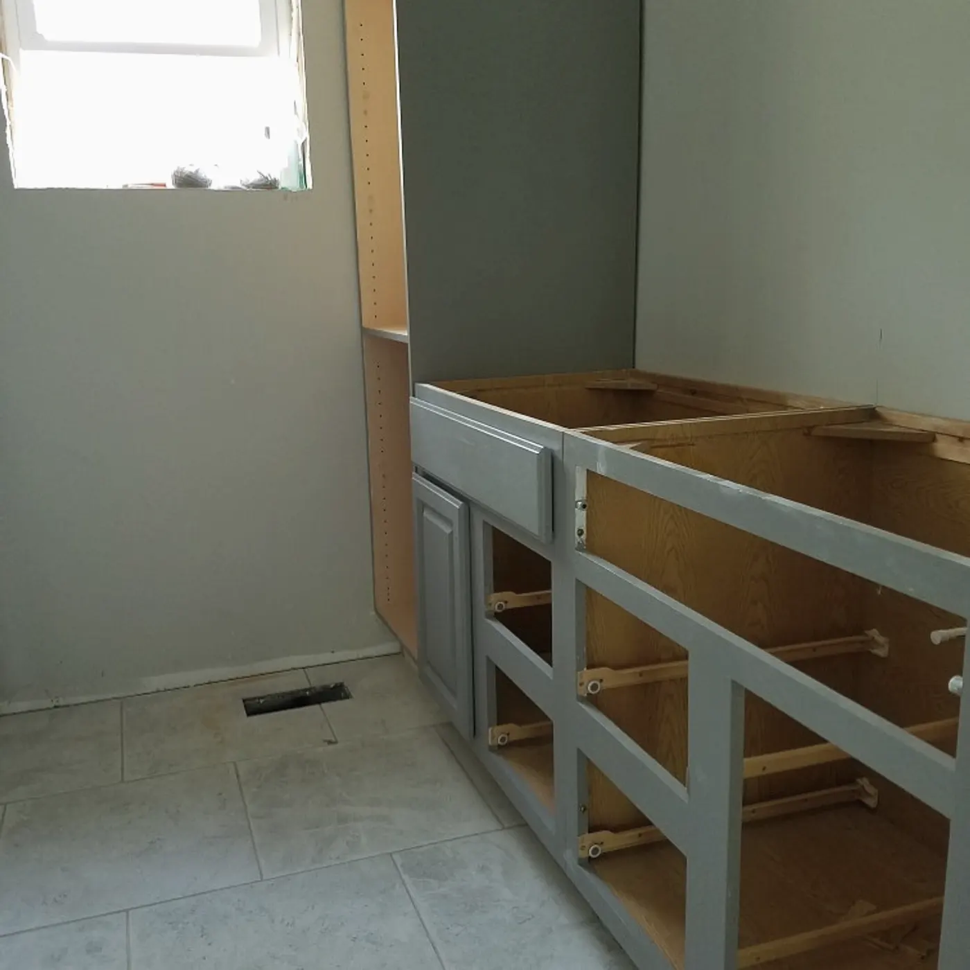 Kitchen base cabinets being set in a new build, drywall finished