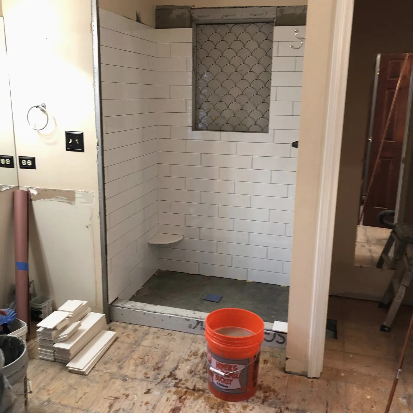 In progress: new white subway tile shower surround with a niche, floor tile being set